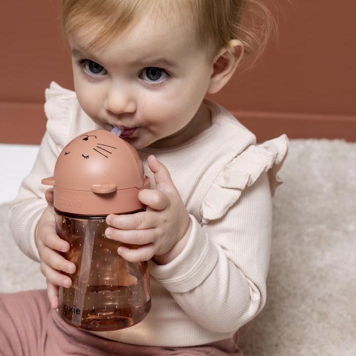Baby holding and drinking from a Trixie Tritan straw cup with a fun animal design of Mrs. Cat.